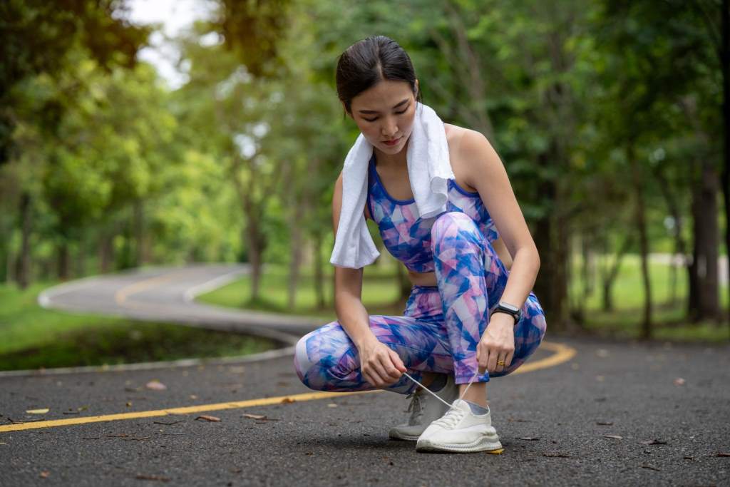 Athletic young woman tying shoelaces before exercising outdoors in a park