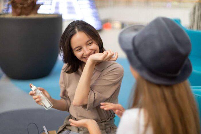 Happy young woman smelling her perfumed hand in shopping mall