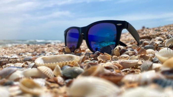 Sunglasses with blue lenses lie on a sandy shell beach on the sea front in sunny weather